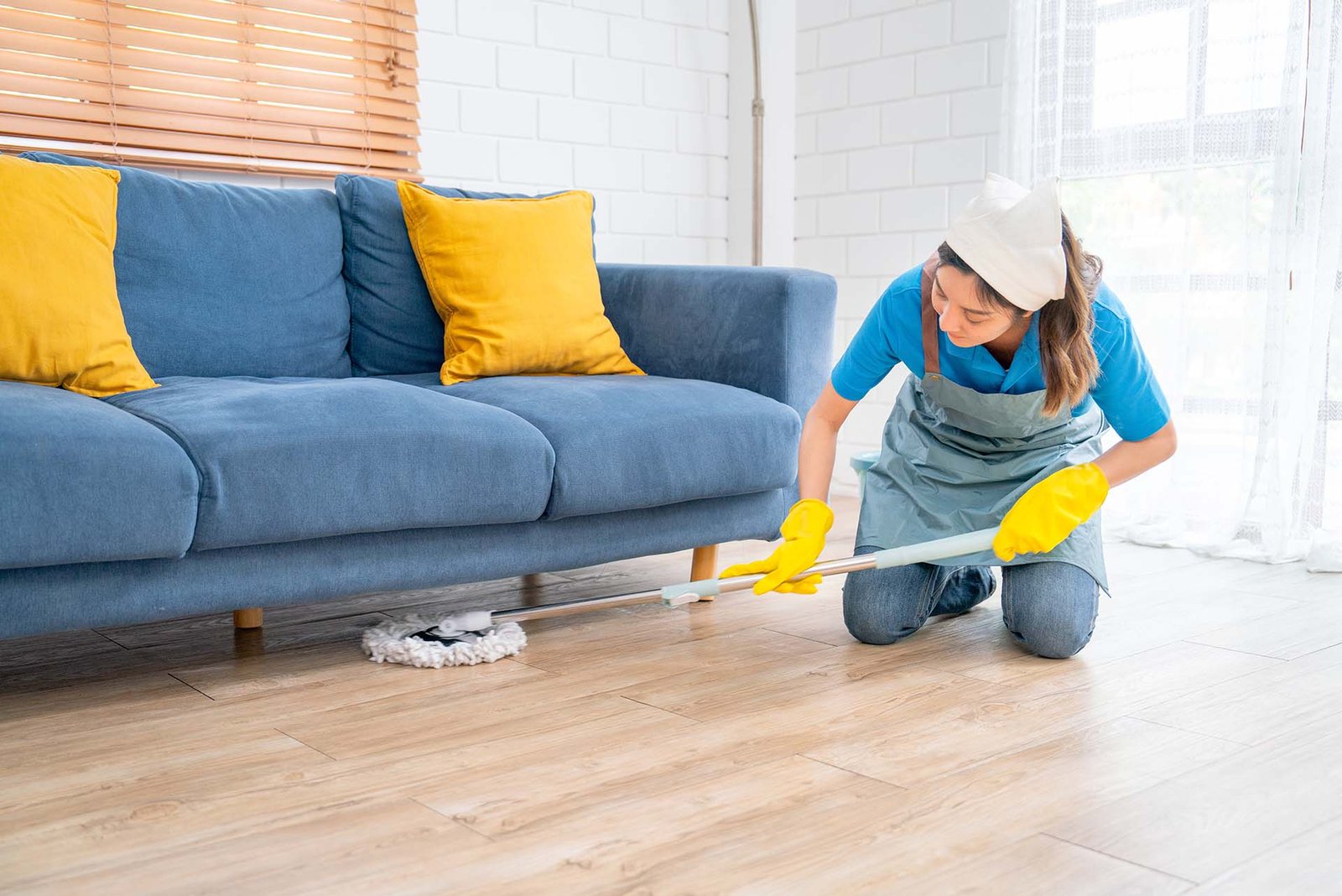 Asian housekeeper or housemaid woman use mop to clean under sofa